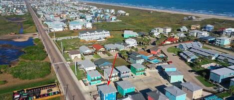 An aerial view of a coastal residential area with houses, a road, and a beach.