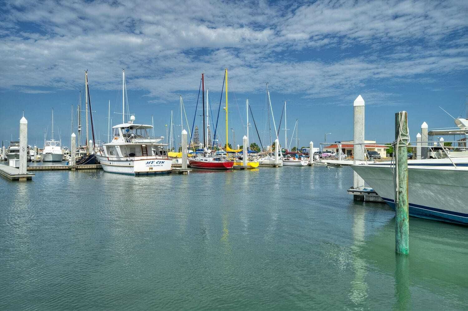 Un port esportiu amb diverses embarcacions amarrades als molls, cel serena i aigua tranquil·la.