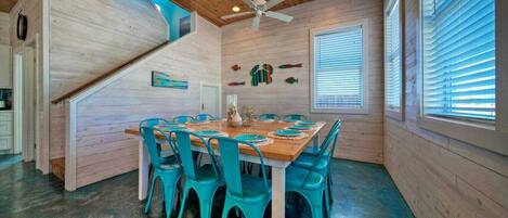 A dining area with a wooden table and turquoise chairs, a ceiling fan, and a staircase leading to an upper level.