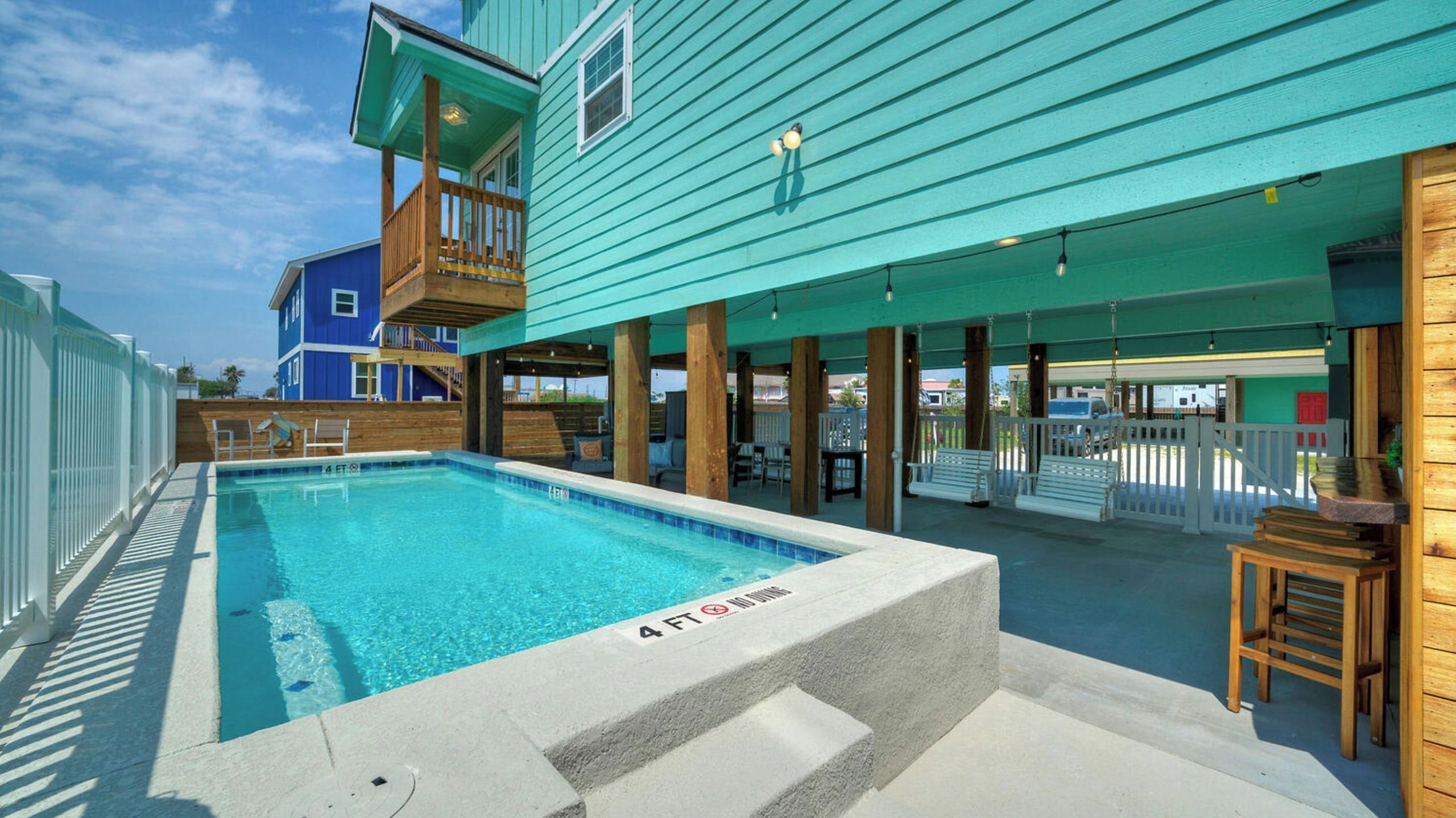 A swimming pool with a 4 ft depth marker, wooden deck, and a covered seating area with benches.