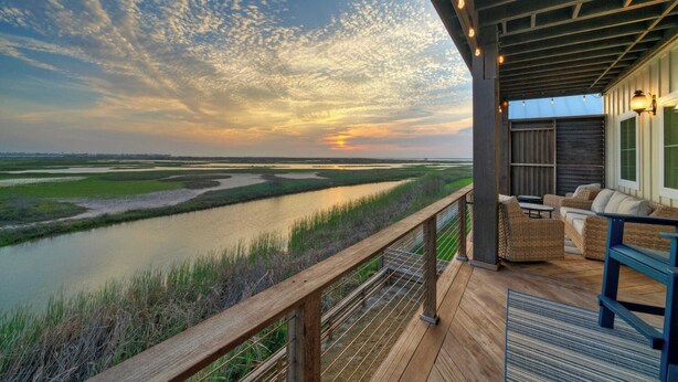 Une terrasse en bois avec des sièges extérieurs, donnant sur une rivière et un paysage marécageux au coucher du soleil.