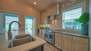 A kitchen with a sink, stove, and cabinets, a window with blinds, and a decorative plant. - Private Pool, Covered Patio 4 Blocks to Beach Bourbon Breeze by Avantstay (Port Aransas)