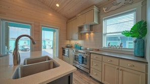 A kitchen with a sink, stove, and cabinets, a window with blinds, and a decorative plant.