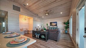 A spacious living area with a wooden ceiling, a dining table set with plates, a sofa, and a television mounted on the wall. - Private Pool, Covered Patio 4 Blocks to Beach Bourbon Breeze by Avantstay (Port Aransas)