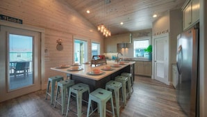 A modern kitchen with wooden walls, a central island with stools, and a stainless steel refrigerator. - Private Pool, Covered Patio 4 Blocks to Beach Bourbon Breeze by Avantstay (Port Aransas)