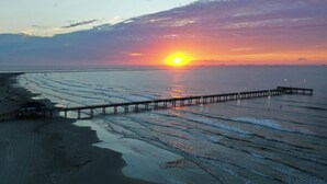 Un atardecer sobre una playa con un muelle que se adentra en el agua.