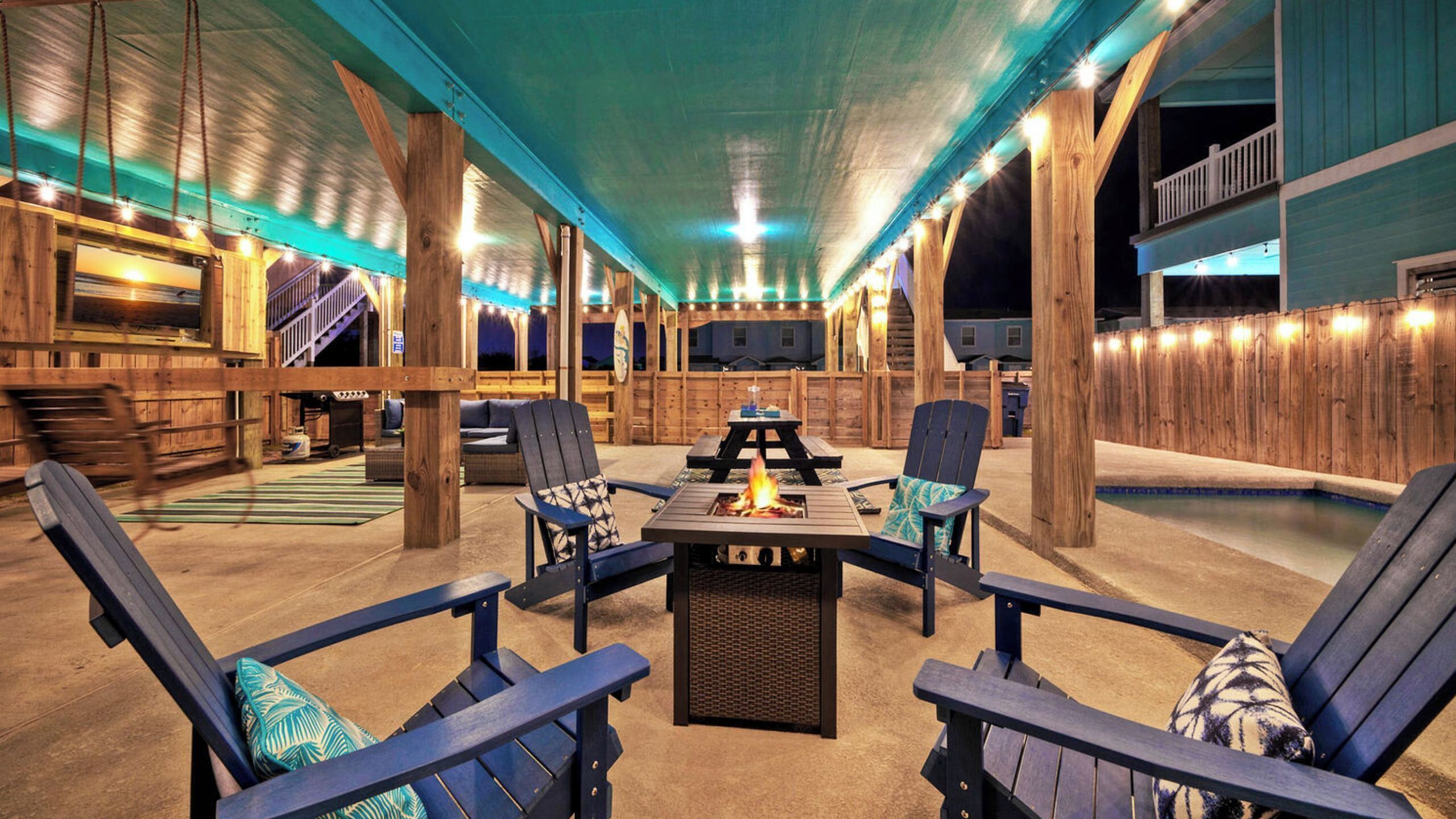 A covered outdoor area with a fire pit, seating, and a pool.