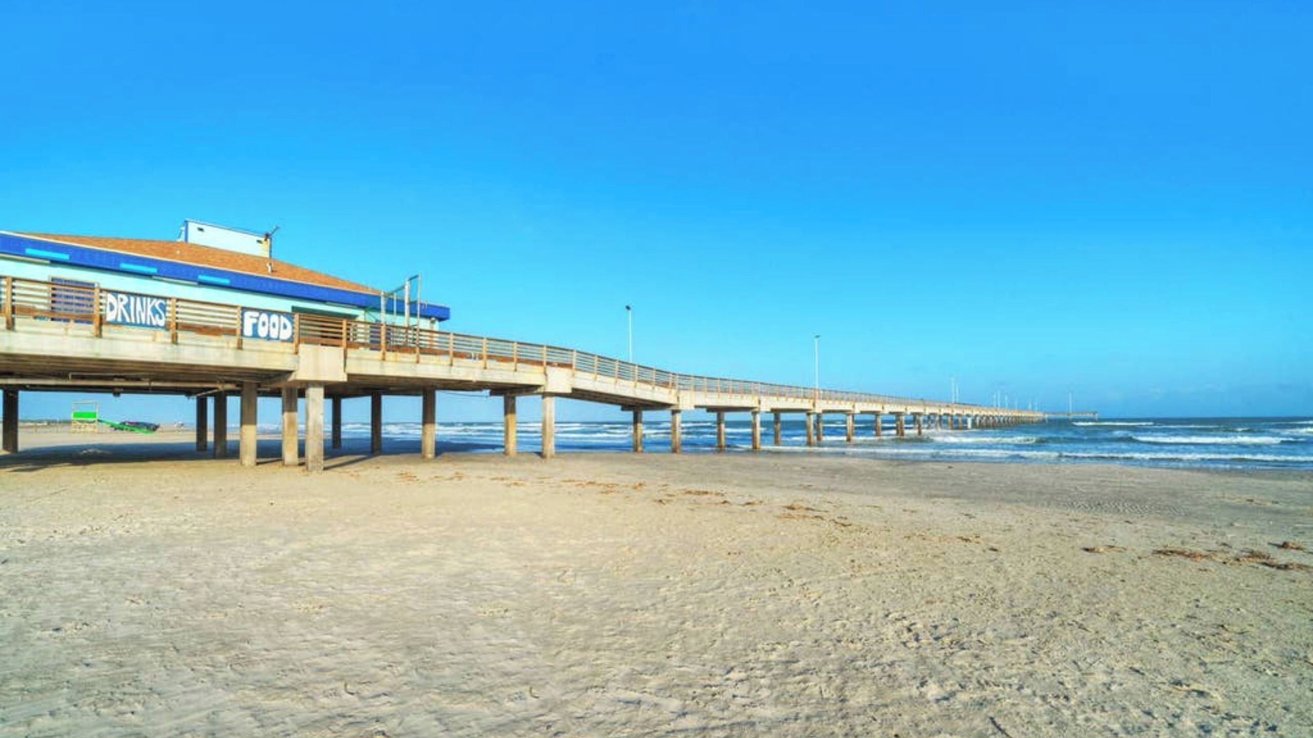 Eine Pier, die sich ins Meer erstreckt, mit einem Gebäude, auf dem 'Drinks Food' steht, auf der linken Seite.