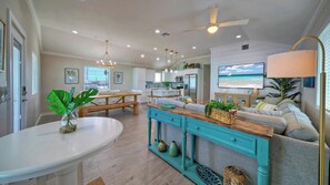 A spacious living area with a kitchen, dining table, and a large TV screen. - Priv Pool, Swing Bar, Ping-pong, Walk to Town Once Upon A Tide by Avantstay (Port Aransas)