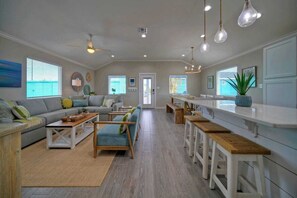 A spacious living area with a sofa set, wooden coffee table, and a dining area with bar stools. - Priv Pool, Swing Bar, Ping-pong, Walk to Town Once Upon A Tide by Avantstay (Port Aransas)