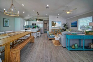 A spacious living area with a wooden dining table, a blue sofa, and a kitchen in the background. - Priv Pool, Swing Bar, Ping-pong, Walk to Town Once Upon A Tide by Avantstay (Port Aransas)