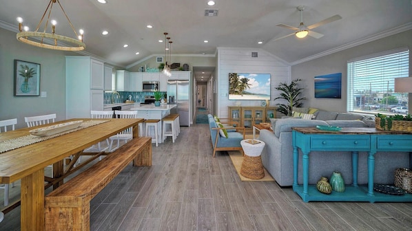 A spacious living area with a wooden dining table, a sofa, and a kitchen in the background.