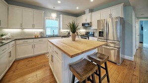 A modern kitchen with white cabinetry, a wooden island, stainless steel appliances, and a chandelier. - Moxy's Beach House by Avantstay Pool + Views (Port Aransas)