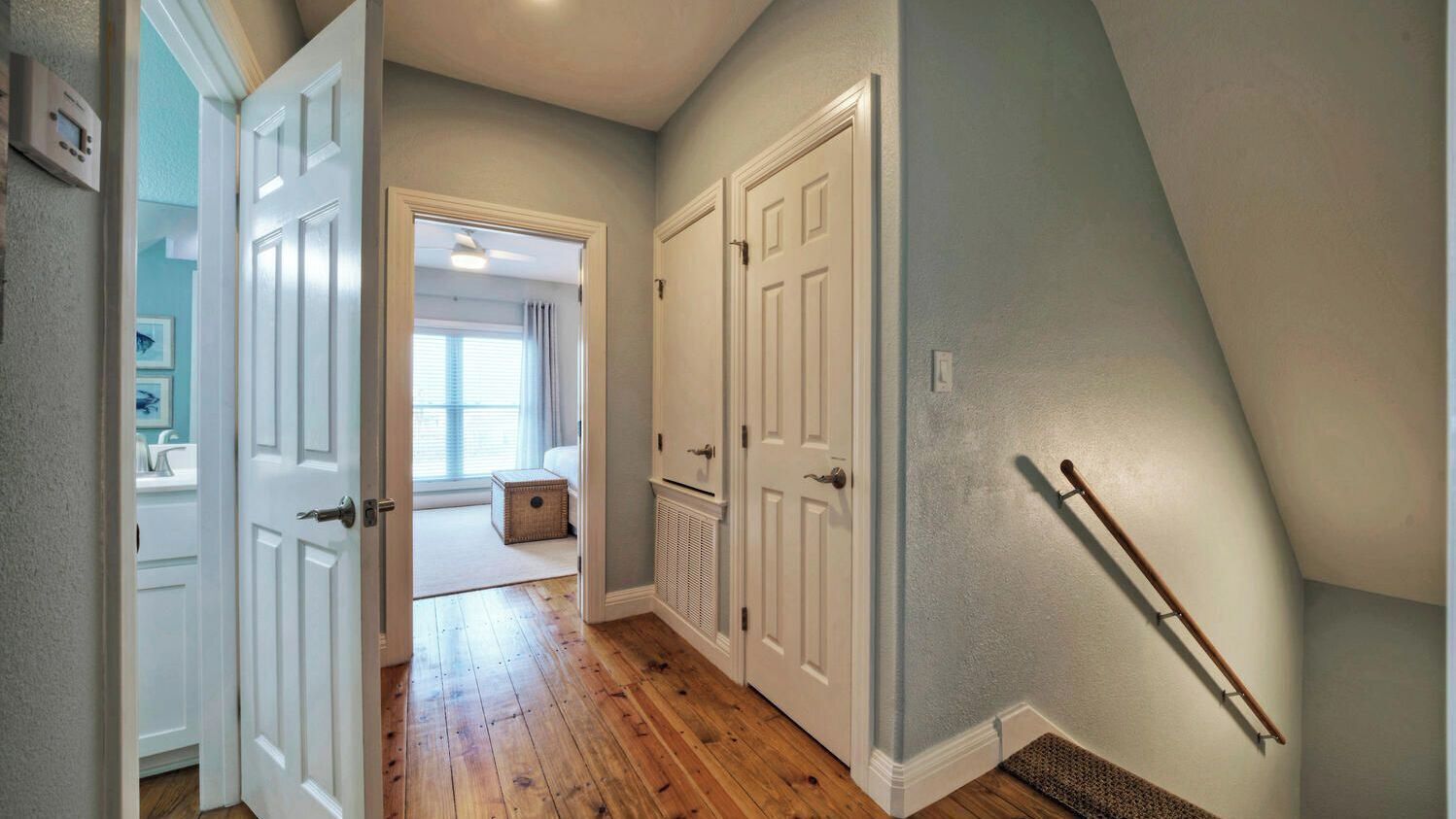 A hallway with wooden flooring, white doors, and a visible staircase.