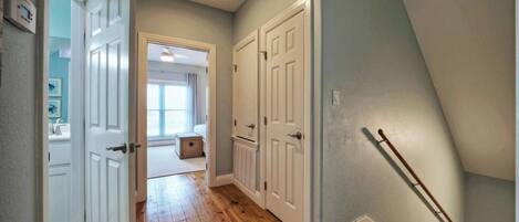 A hallway with wooden flooring, white doors, and a visible staircase.