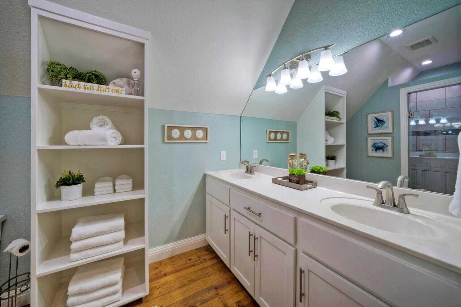 Une salle de bain moderne avec un grand meuble-lavabo, des étagères avec des serviettes et un miroir avec éclairage intégré.