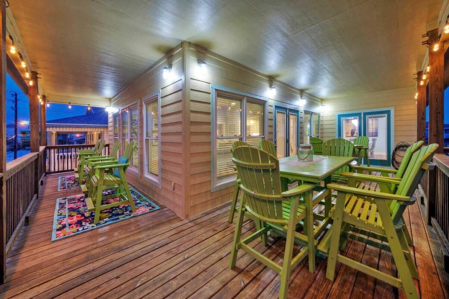 A covered outdoor area with wooden deck, green chairs, and a table.
