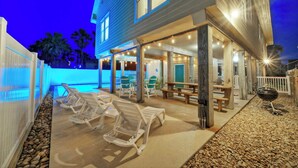 A poolside area with lounge chairs, a barbecue grill, and a covered patio with tables and chairs. - Moxy's Beach House by Avantstay Pool + Views (Port Aransas)