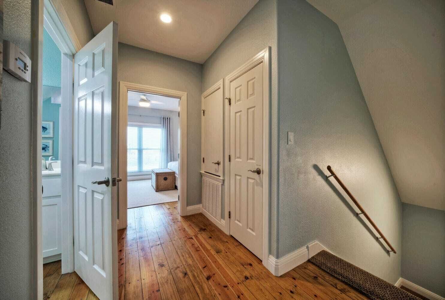 A hallway with wooden flooring, white doors, and a handrail on the right wall.