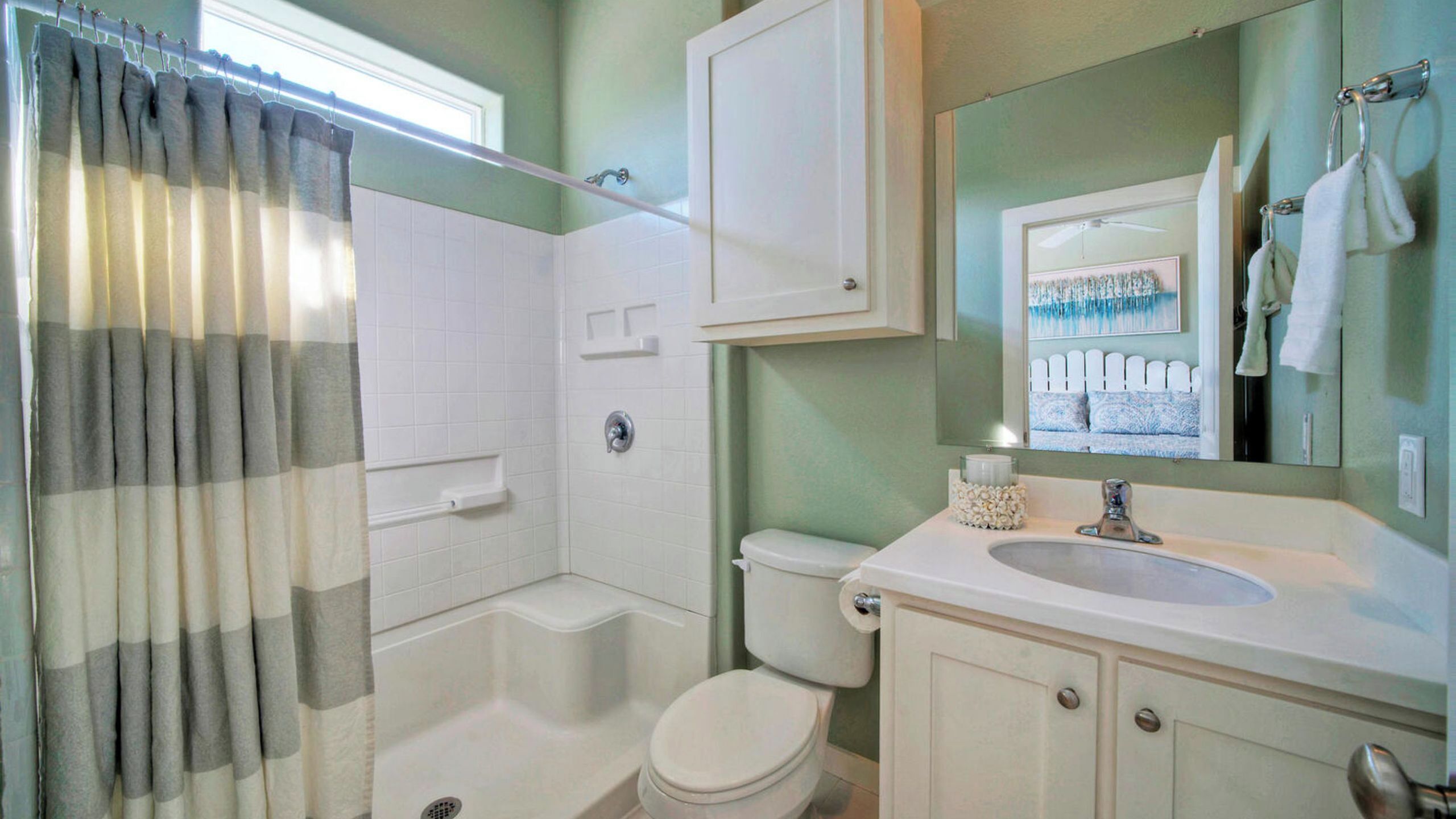 A bathroom with a shower, toilet, sink, and a mirror.