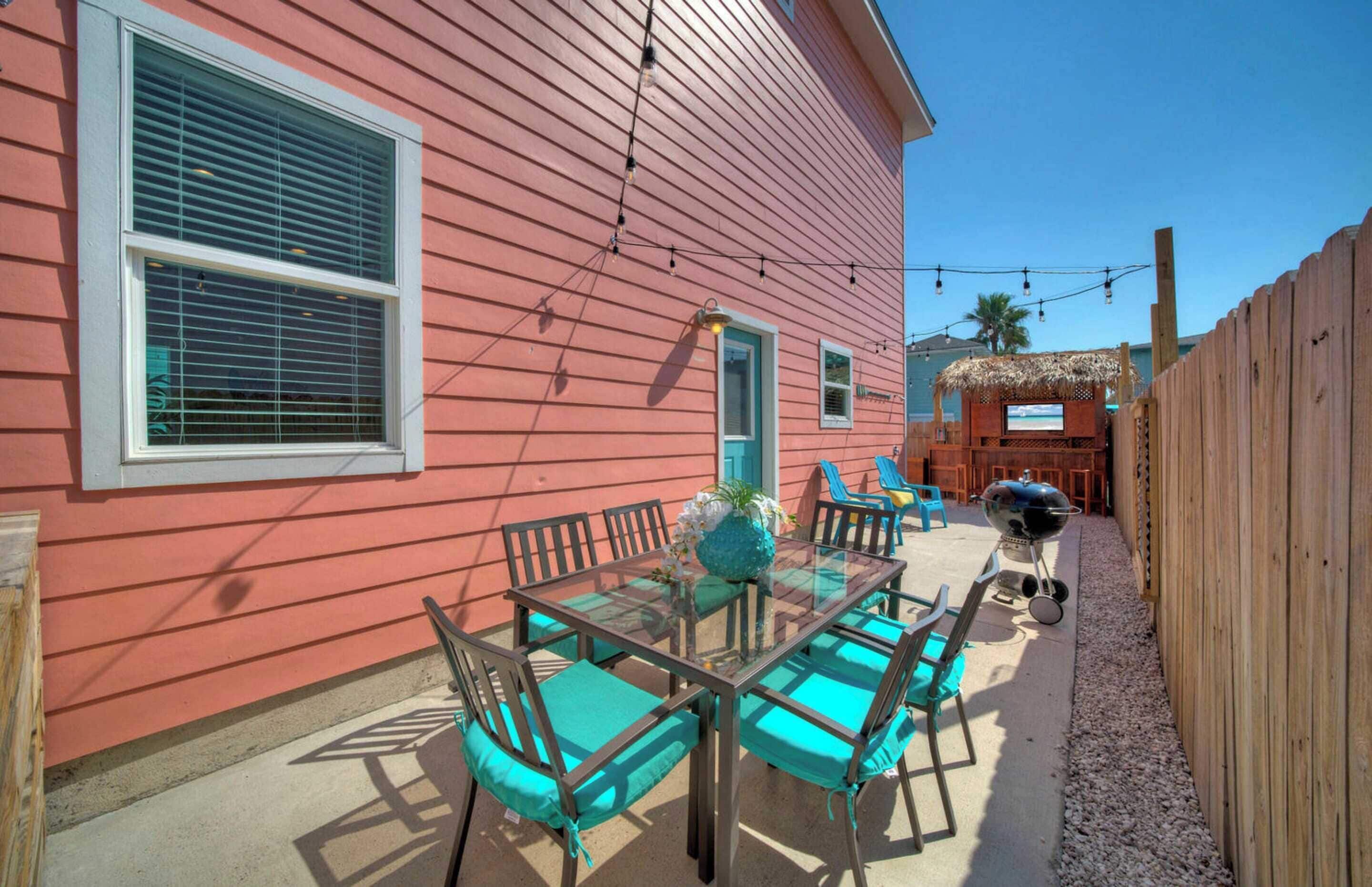 A glass-top patio table with chairs, a barbecue grill, and a tiki hut.
