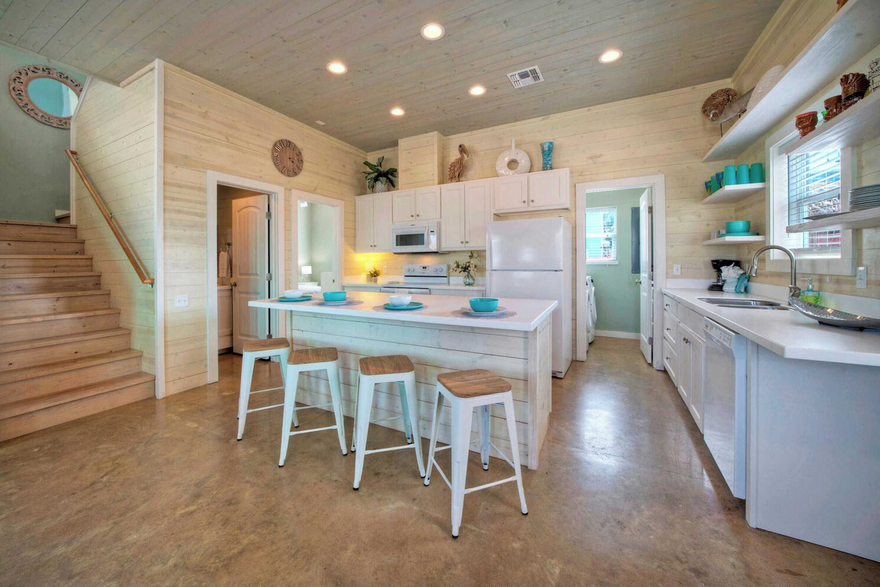 A kitchen with white cabinets, a central island with stools, a microwave, and a refrigerator.