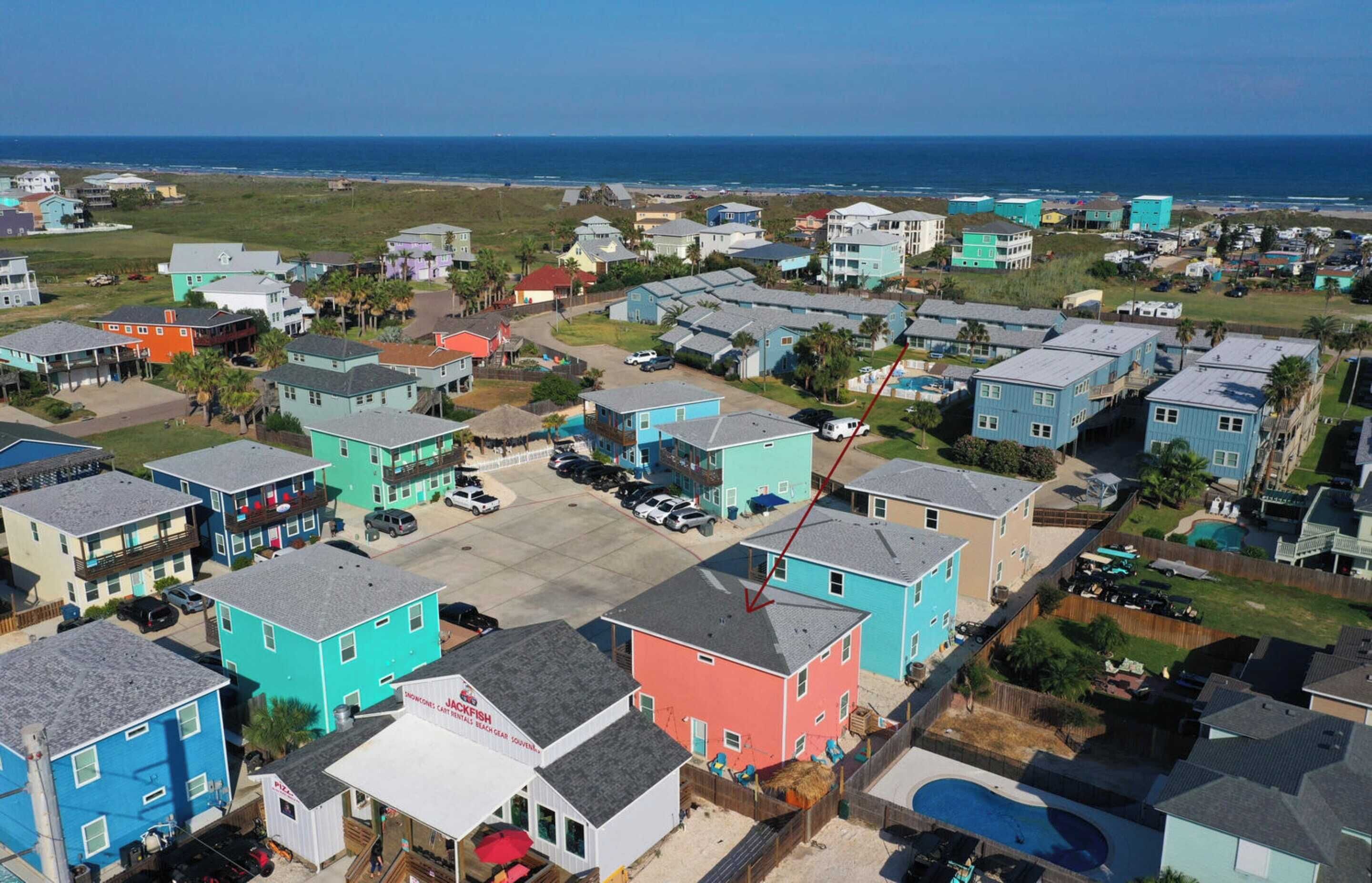 A coastal residential area with colorful houses, a clear view of the ocean, and a parking lot.