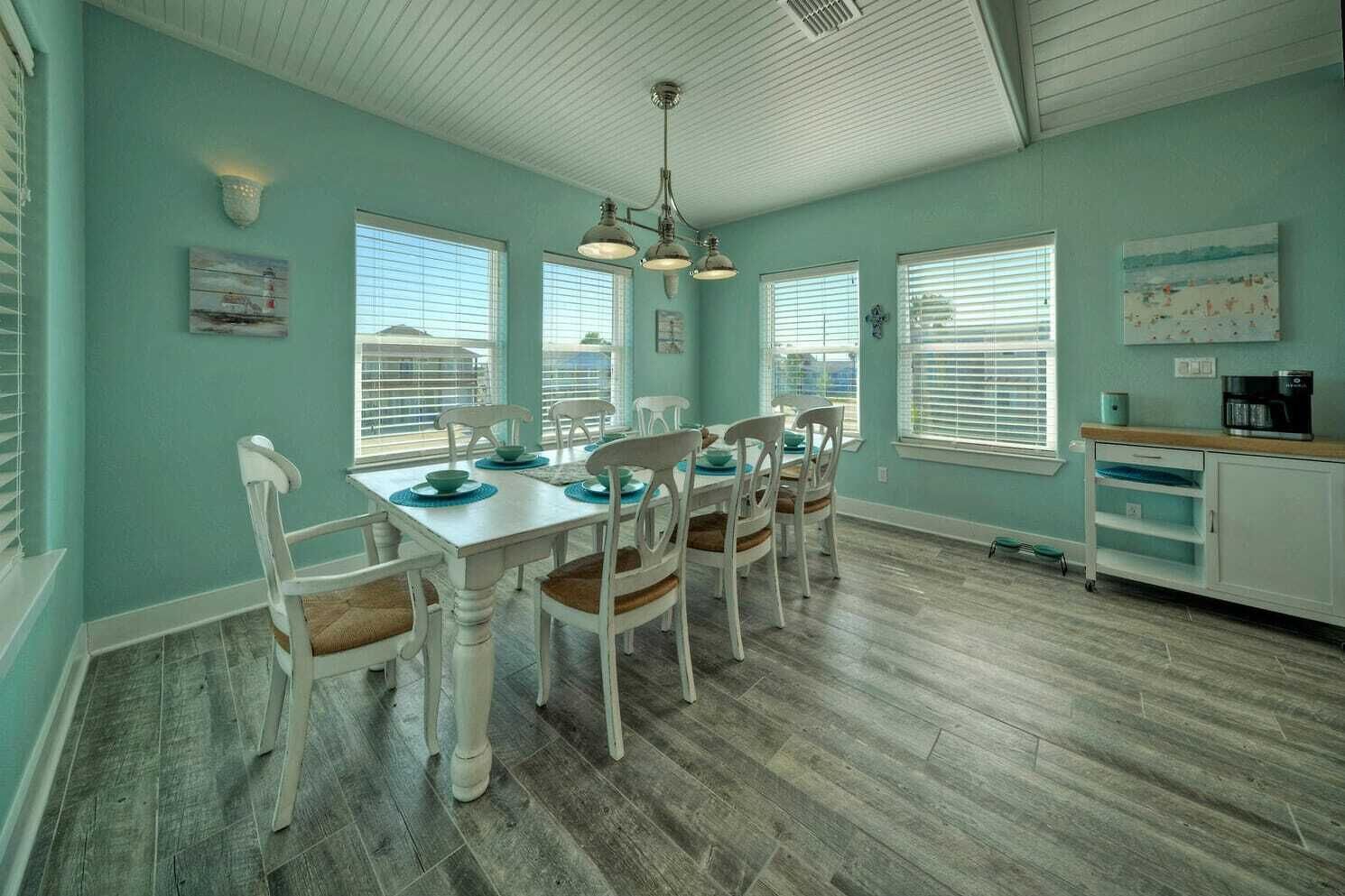 Un coin repas avec une table et des chaises blanches, des murs de couleur turquoise et un plancher en bois.