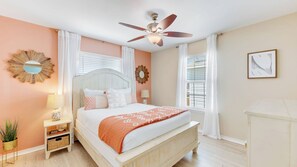 Une chambre à coucher comprenant un lit, un ventilateur de plafond, une table de chevet avec une lampe et un miroir fixé au mur.