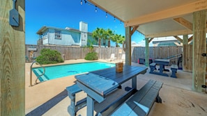 A backyard with a swimming pool, wooden deck, and a covered patio area.