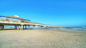 A pier extending over a sandy beach with a building labeled 'DRINKS' and 'FOOD' on the left.
