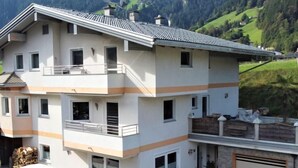 A two-story building with a balcony, a garage, and a view of a green valley. - Apartment Franz by Interhome (Hippach)