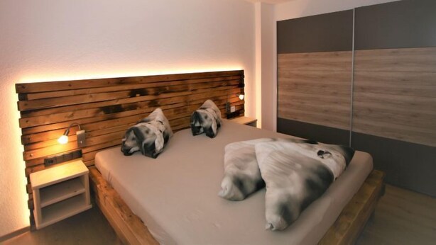 A modern bedroom with a wooden headboard, a bed with two pillows, and a bedside table with a lamp. - Apartment Franz by Interhome (Hippach)