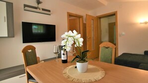 A dining area with a wooden table, two chairs, a TV mounted on the wall, and a potted orchid on the table. - Apartment Franz by Interhome (Hippach)