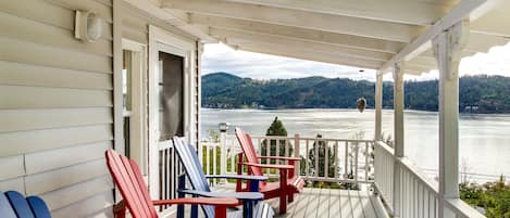 Una terraza de madera con sillas Adirondack y vistas a un lago y colinas.