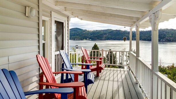 Una terraza de madera con sillas Adirondack y vistas a un lago y colinas.