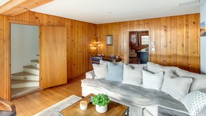 Una habitación con paneles de madera, un sofá, una mesa de centro con una planta y una escalera.