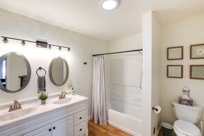 Een badkamer met twee wasbakken, een douche, een toilet en kunstwerken in lijsten aan de muur.