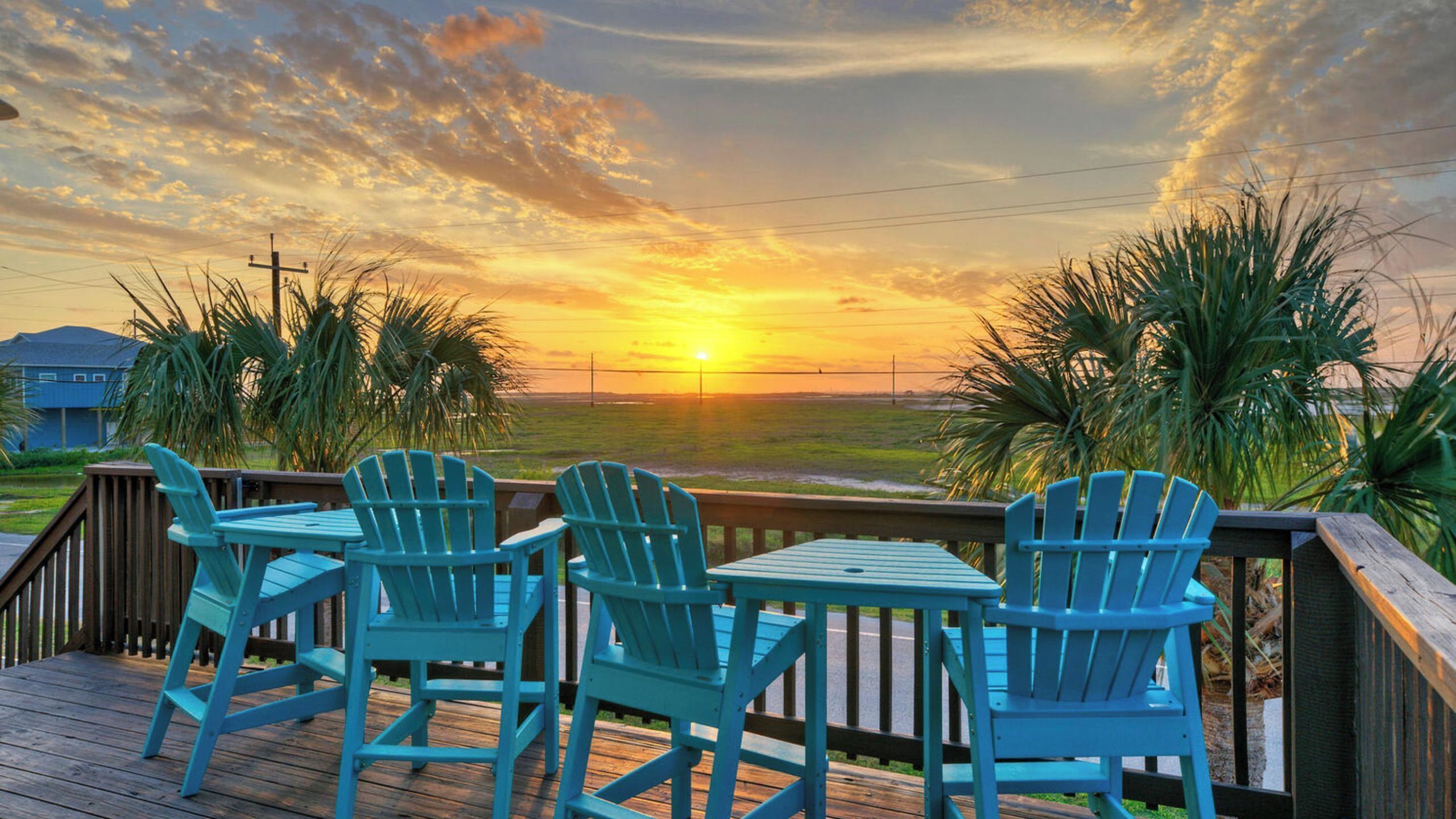 A deck with chairs and a table, overlooking a sunset over a flat landscape.