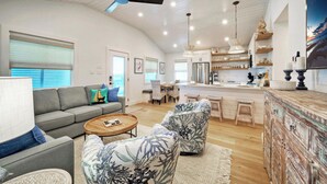 A spacious living area with a sofa, two armchairs, a coffee table, and a kitchen area with a bar. - Boujee Pelican by Avantstay Pool+game Room+views (Port Aransas)