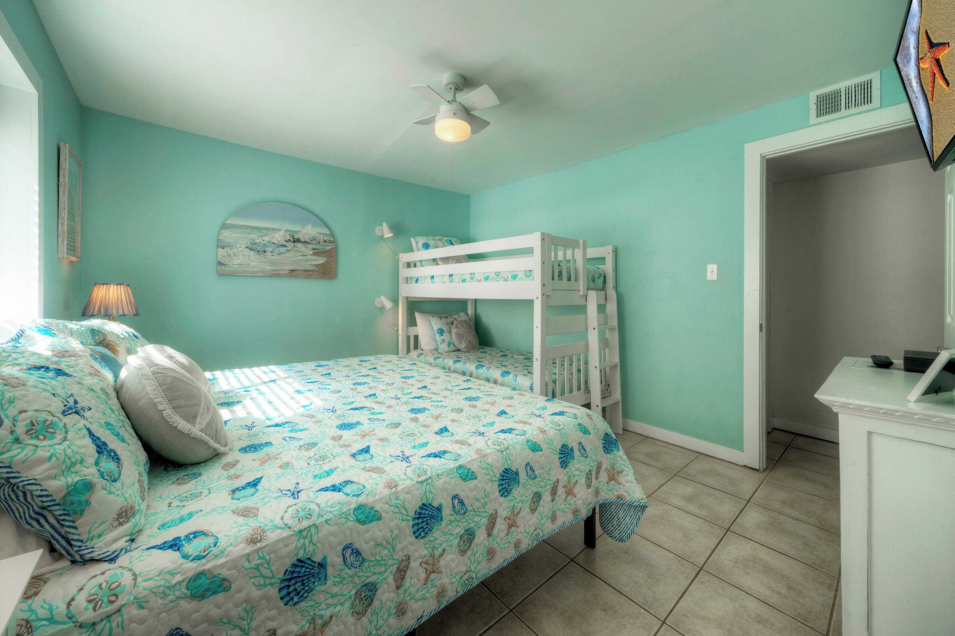 A bedroom with a bunk bed, a ceiling fan, and a door leading to another room.
