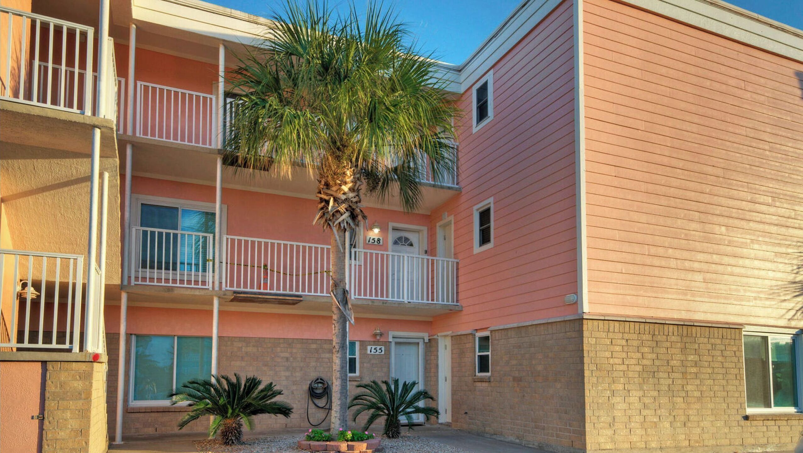 A multi-story building with balconies, a palm tree, and a brick facade.