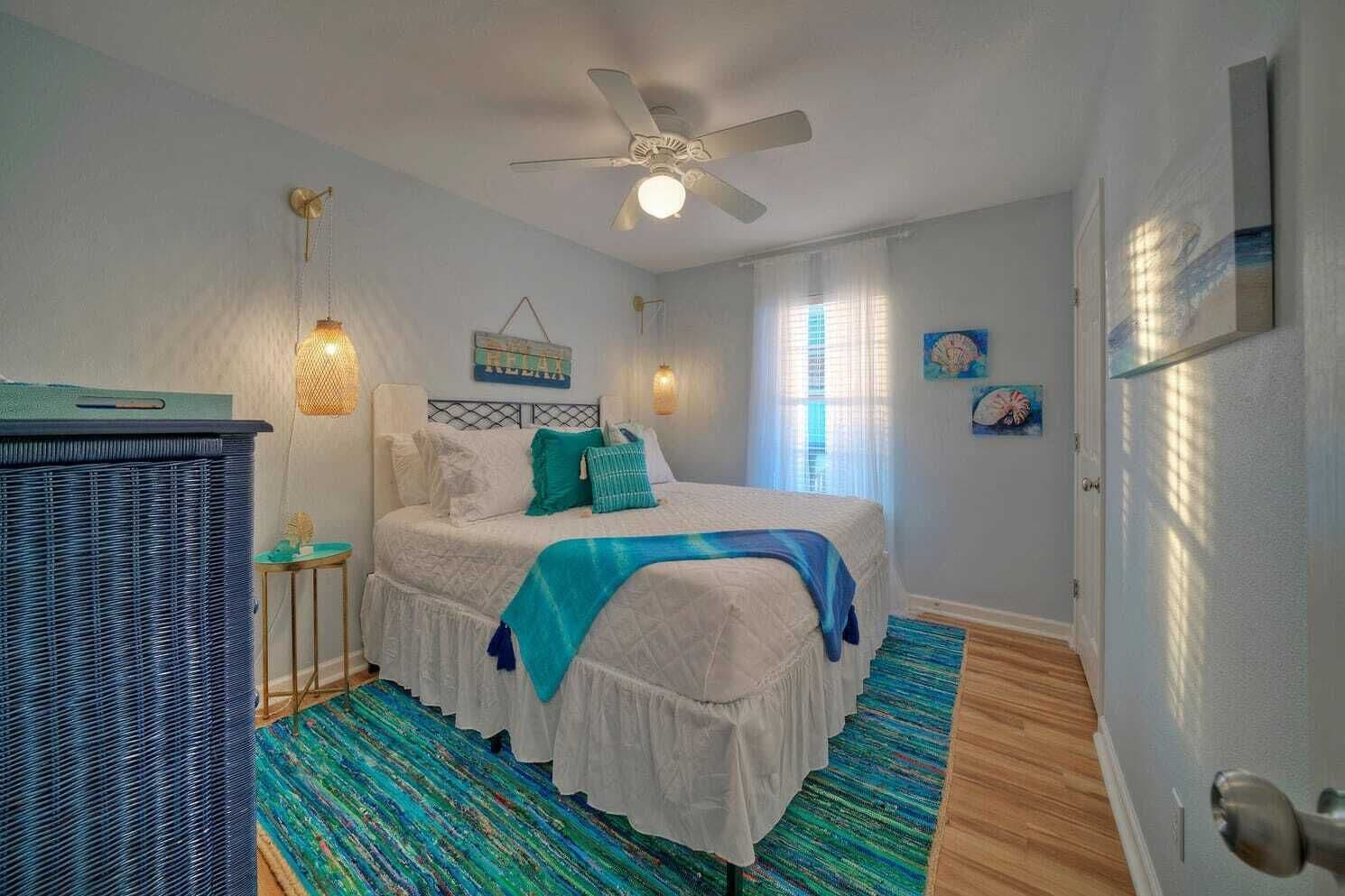 Une chambre à coucher avec un lit, un ventilateur de plafond, une fenêtre avec des rideaux et une porte.