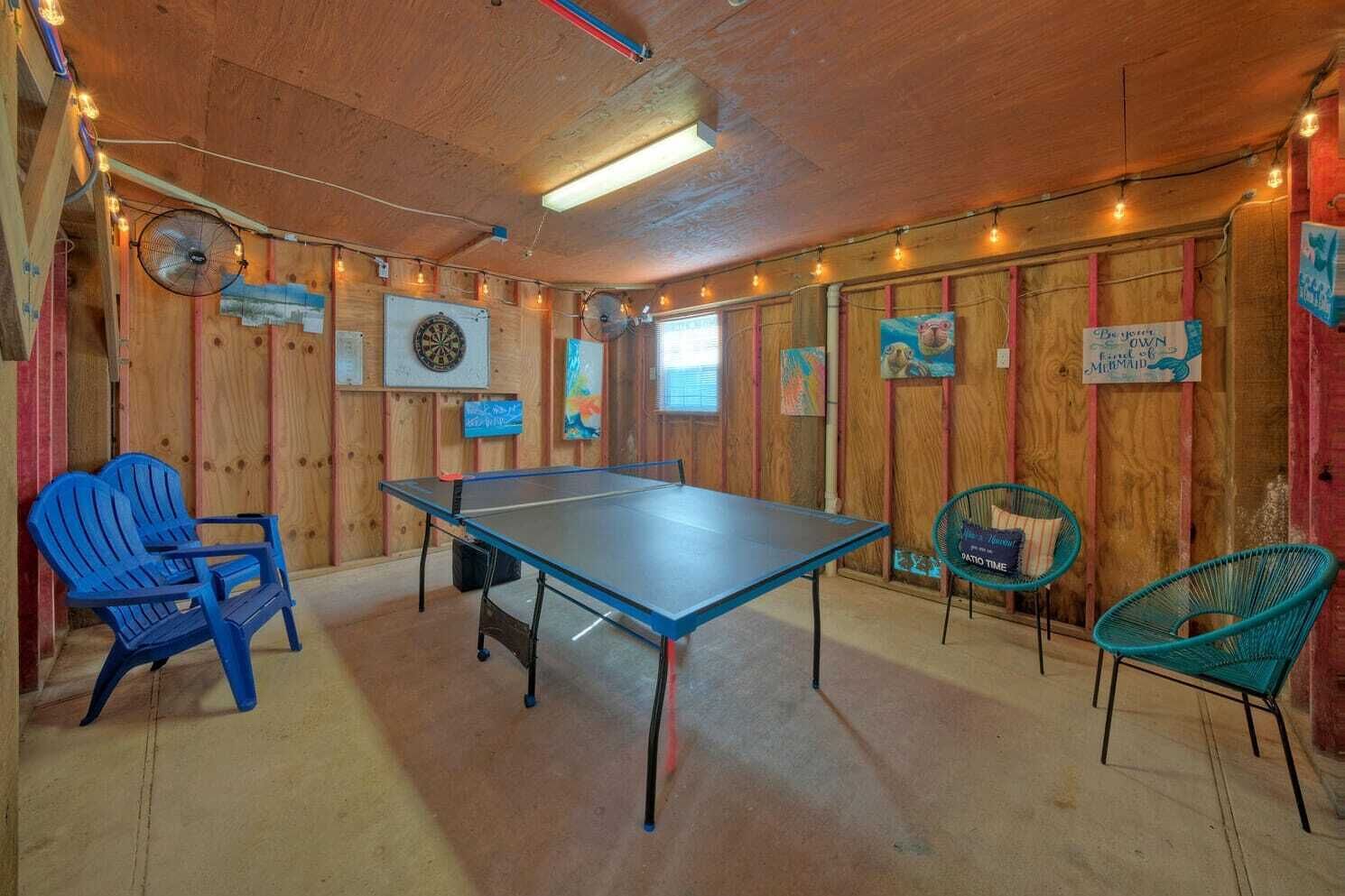 A room with a ping pong table, two blue chairs, and two teal chairs.