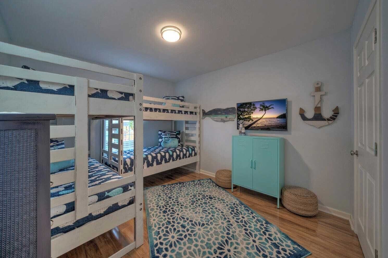 Une chambre avec des lits superposés, une armoire turquoise, un tapis à motifs et une décoration sur le thème de la marine.
