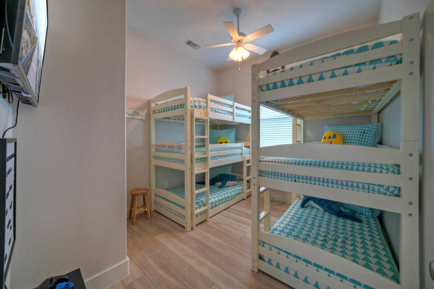 A room with bunk beds, a ceiling fan, and a small stool.