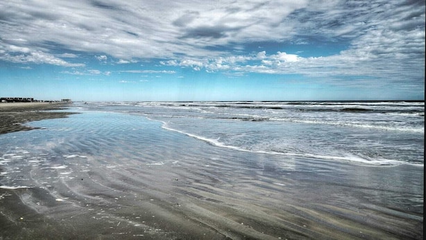 Een strand met golven, een heldere lucht en een verre kustlijn met gebouwen.