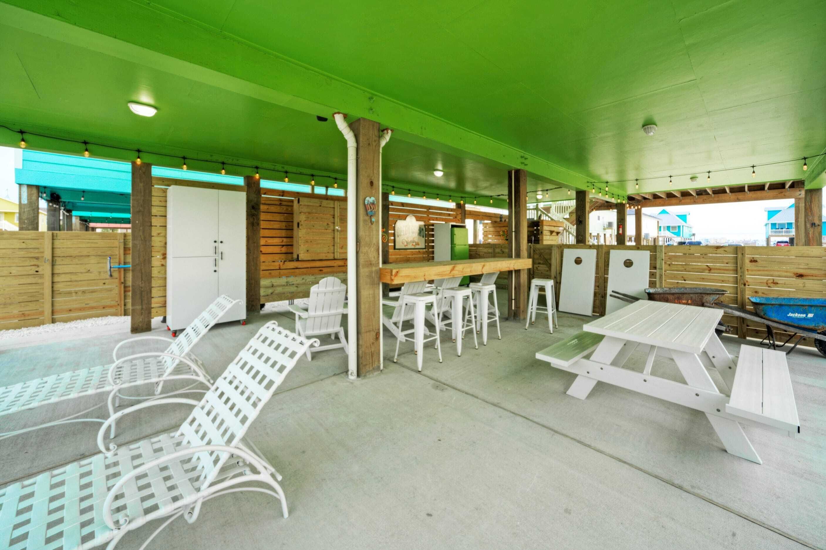A covered outdoor seating area with white metal chairs and tables, wooden walls, and a green ceiling.