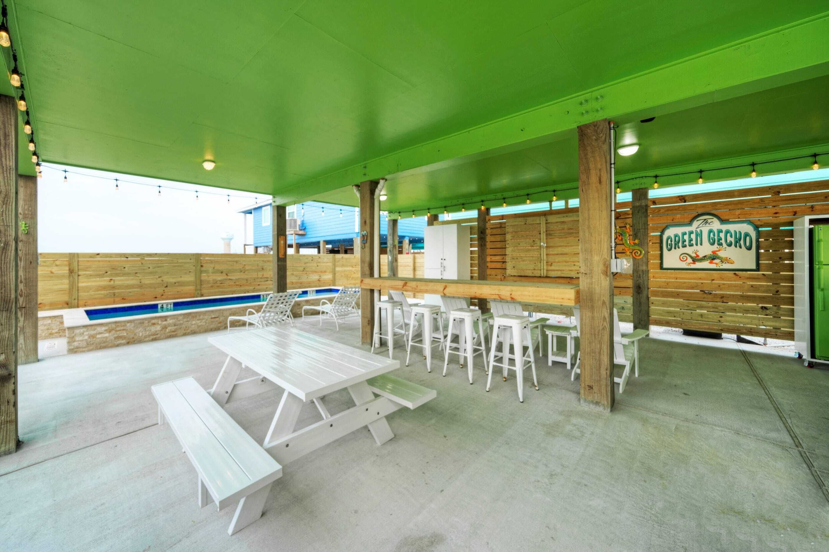 Un patio al aire libre con mesas y sillas de picnic, una piscina y un letrero que dice 'The Green Gecko'.