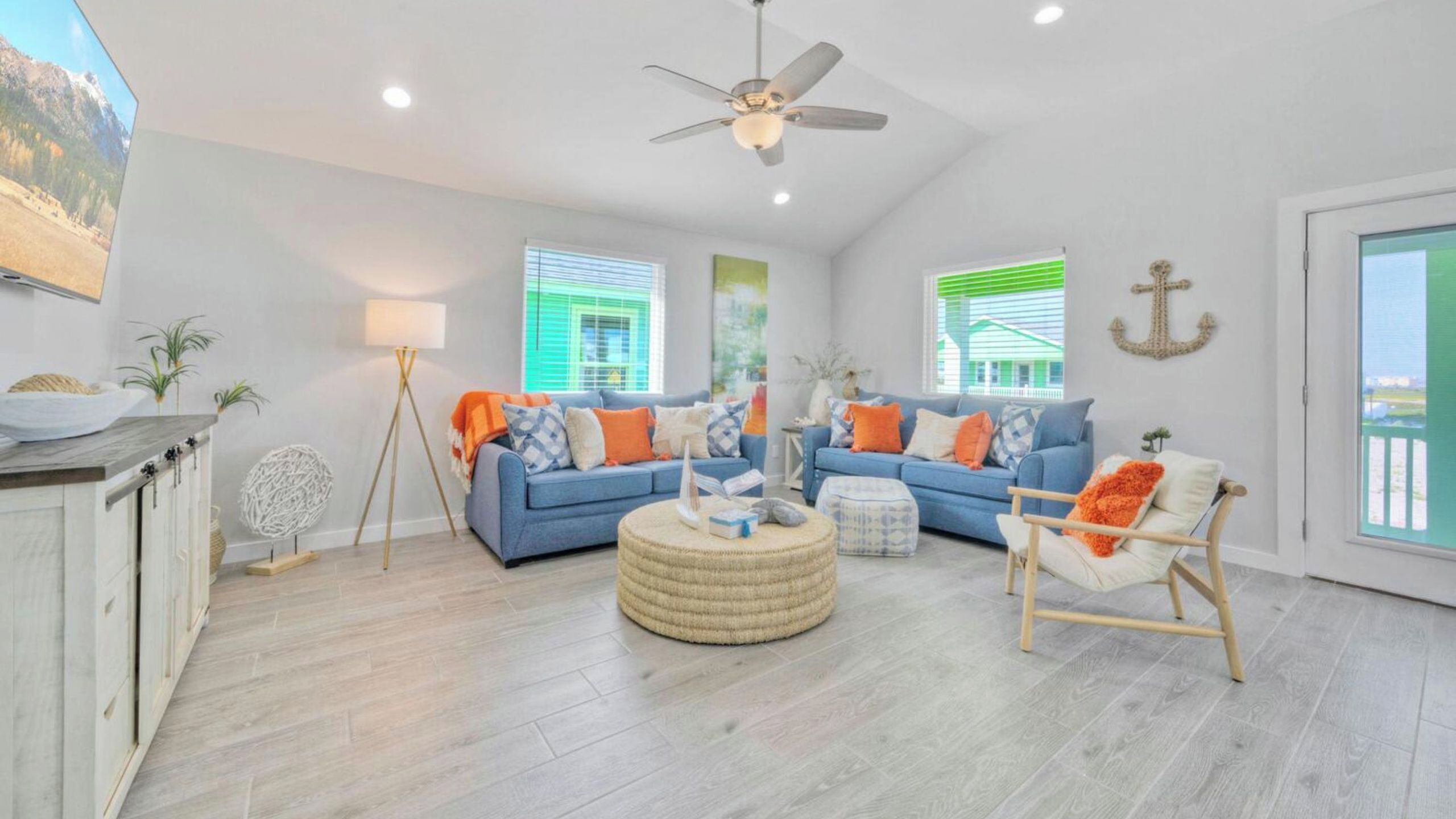 A spacious living room with a ceiling fan, two sofas with colorful cushions, a round ottoman, and a wooden chair.